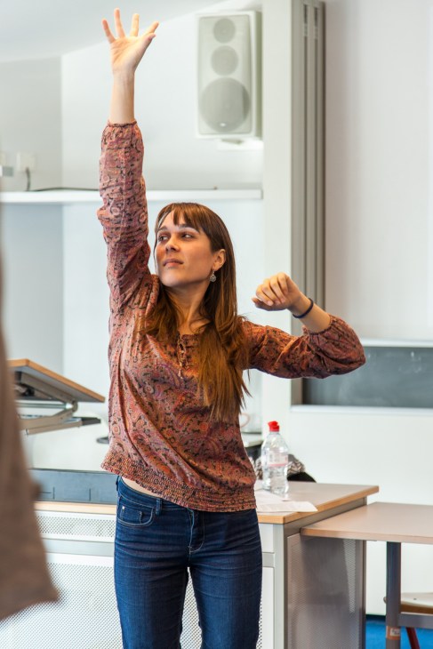 Woman with raised arm performs a stretching exercise during a voice-training workshop at interpreter school.