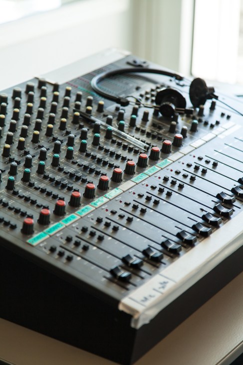 Close-up of an interpretation console with multiple faders, buttons and headphones used for training.