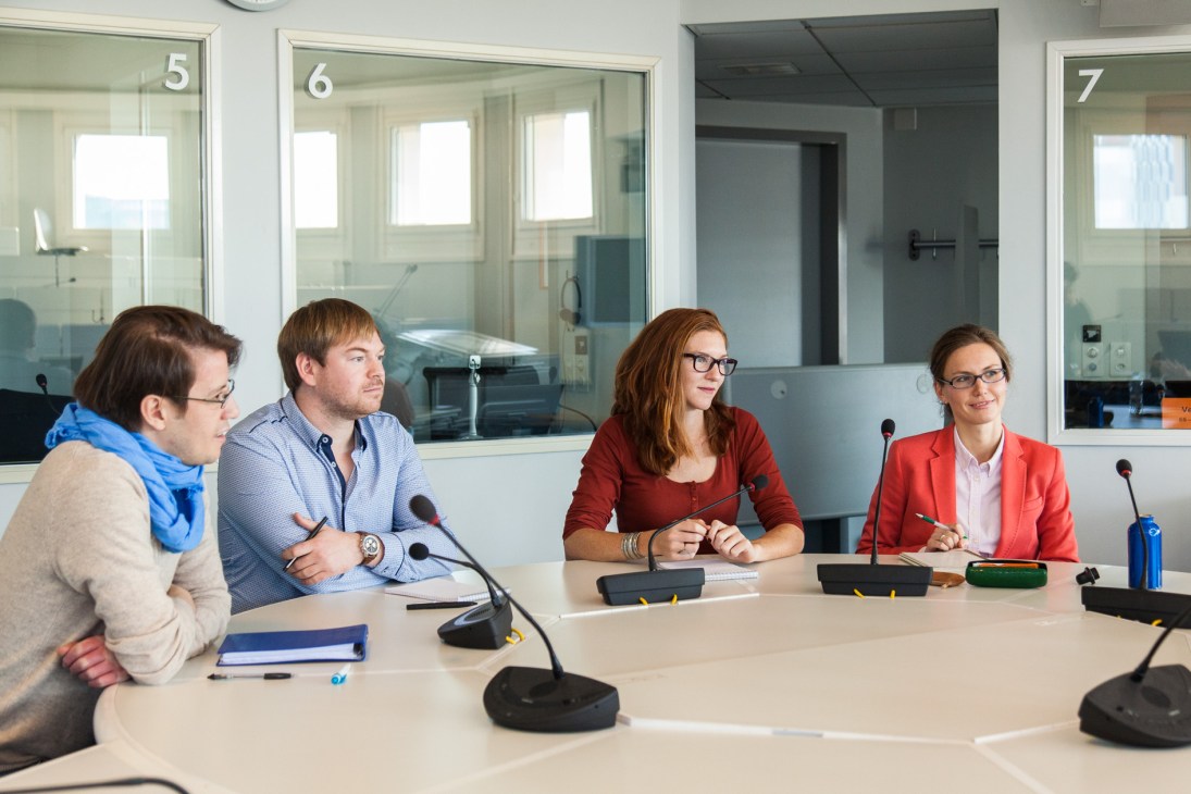 Four students seated at a conference table with microphones during interpreter training at the University of Geneva.