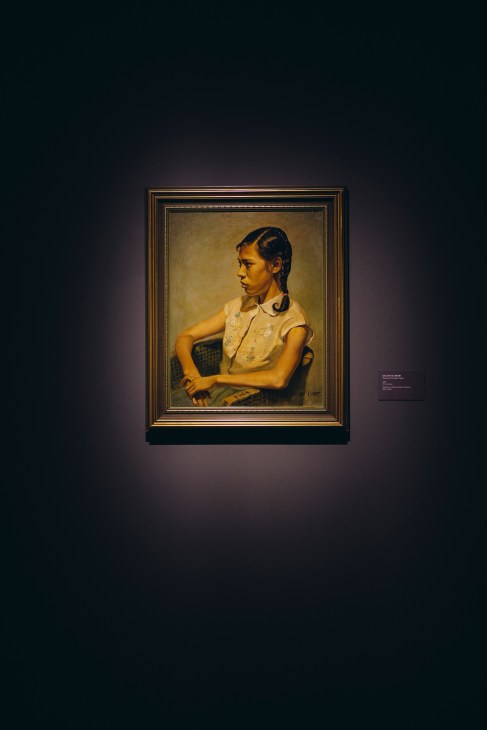 Portrait of a young woman in a yellow blouse seated and gazing to the side, displayed in a gold-framed painting at National Gallery Singapore.