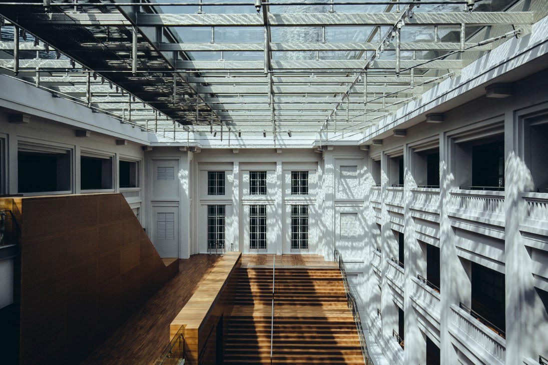 Courtyard with glass roof structure casting geometric shadows on wooden flooring and white walls.