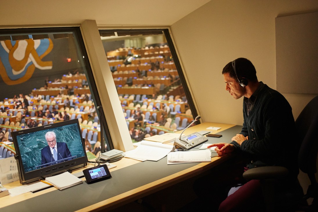 Spanish booth interpreter Aitor Arauz wearing headphones while working at a desk overlooking the UN General Assembly Hall.