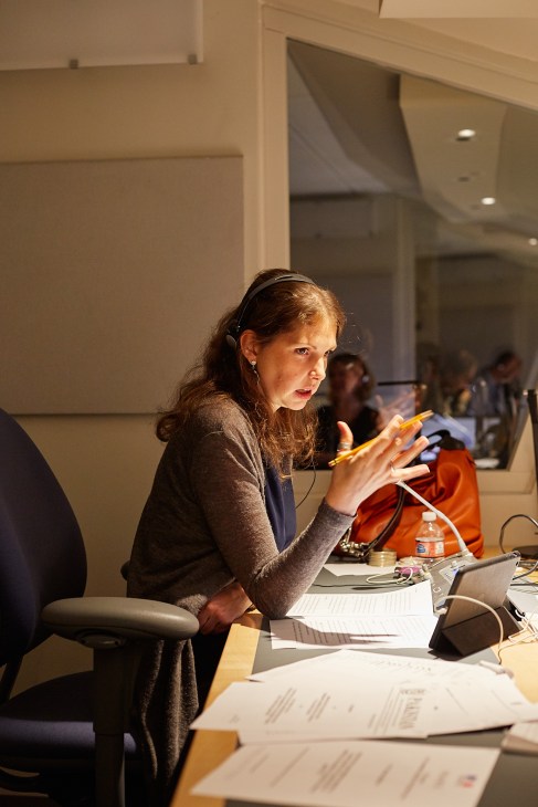 French interpreter Véronique Vandegans speaks during a voice-training workshop, wearing headphones and gesturing expressively at a conference table.