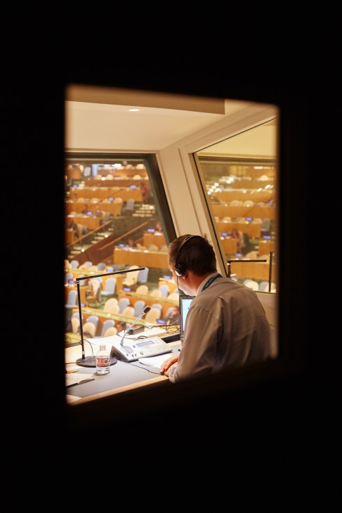 UN interpreter wearing headphones works in booth overlooking General Assembly Hall