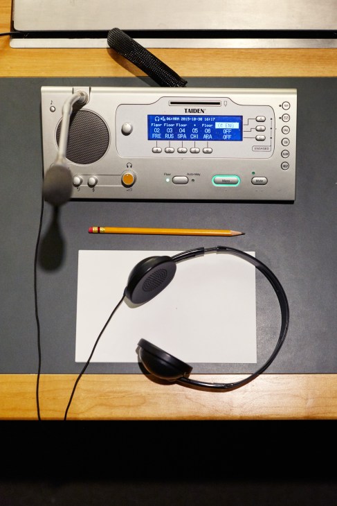 Taiden interpretation equipment displaying language channels on a blue screen with headphones and microphone on wooden desk.