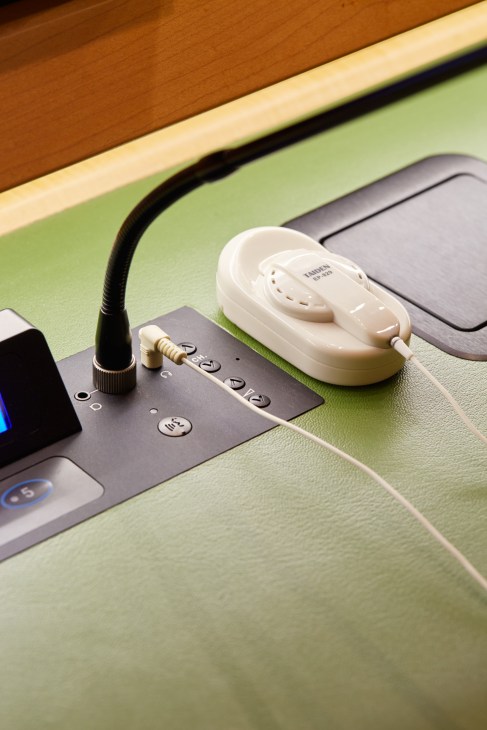 Close-up of white Taiden earpiece and black microphone on green interpreter booth desk.