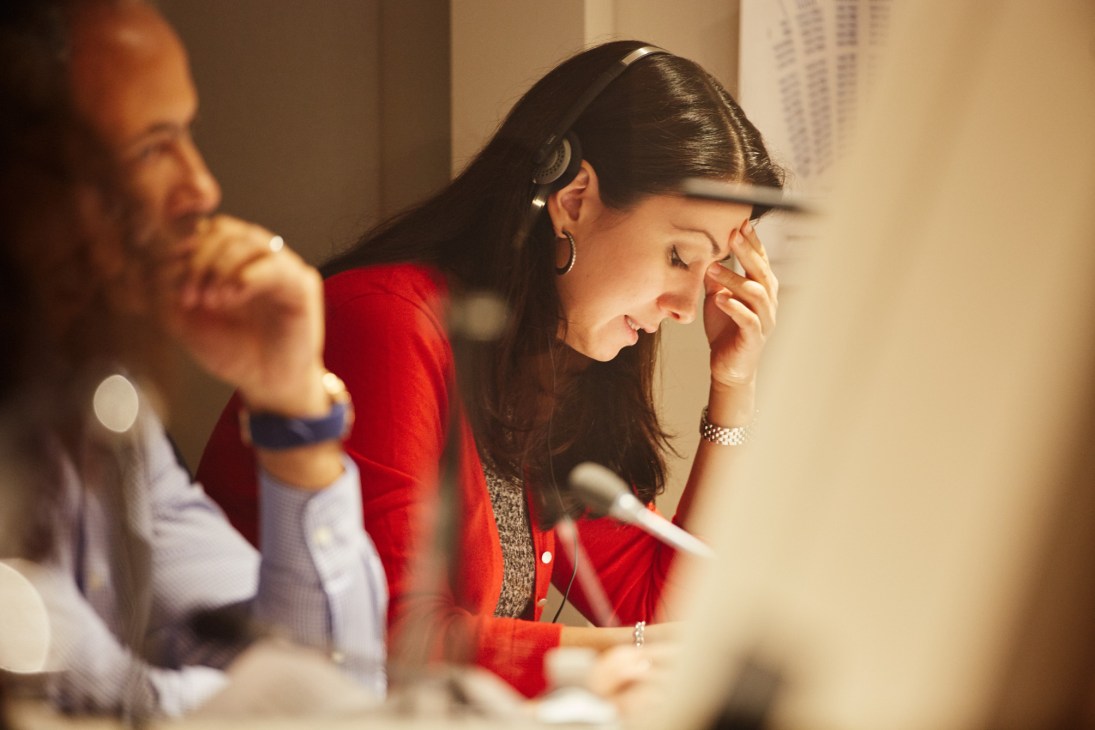 Woman in red shirt concentrating during interpretation training session with colleagues at table.