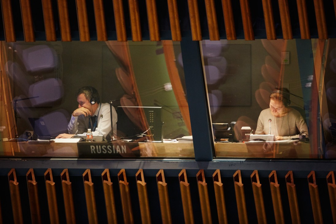 Two interpreters wearing headsets sit in the Russian interpretation booth above the UN General Assembly Hall.