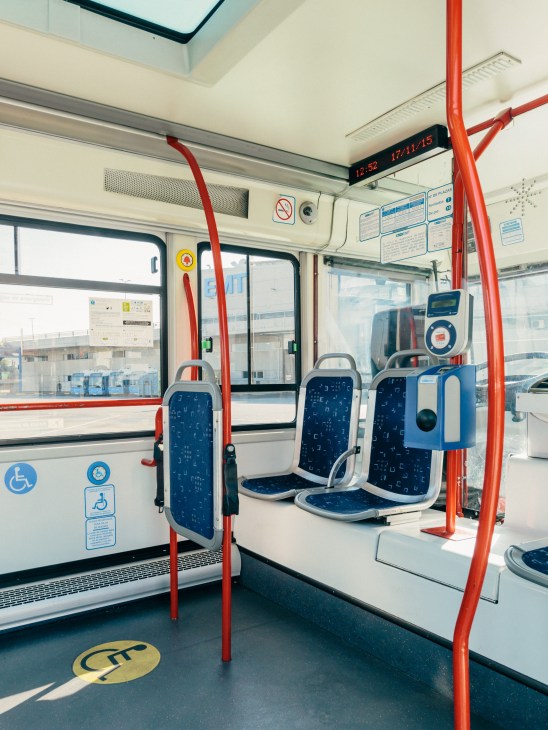 Interior of the EMT Gulliver bus with blue patterned seats, red support poles and windows showing city buildings.