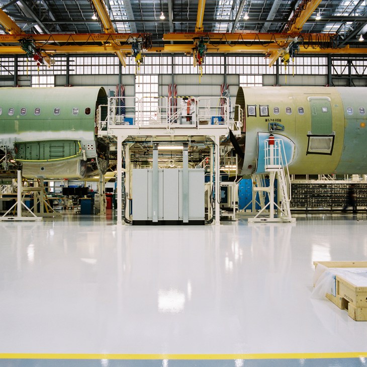 Airbus A320 aircraft fuselage under assembly with yellow overhead cranes in factory.