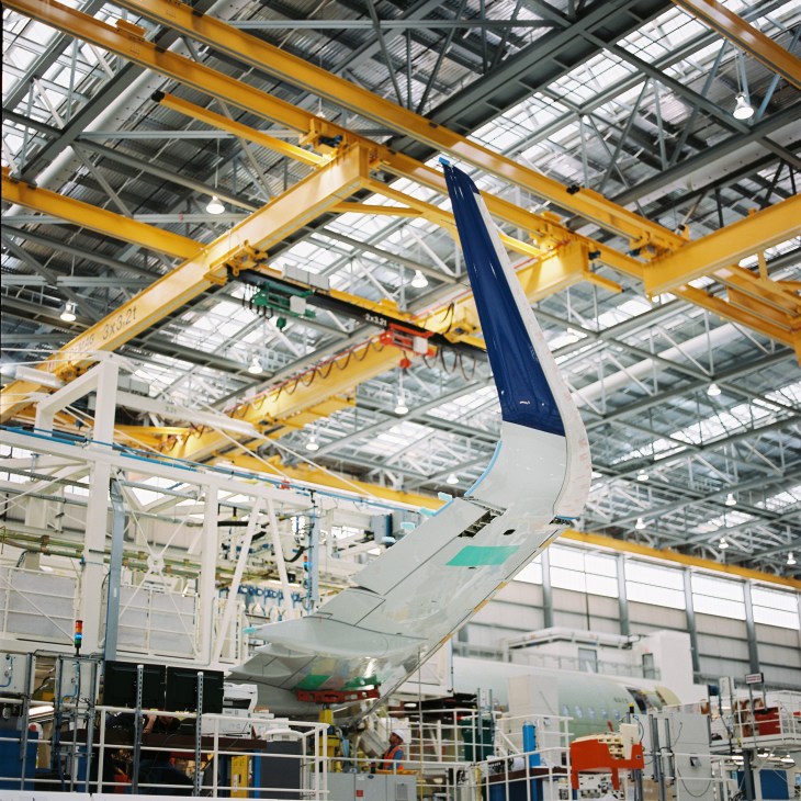 Airbus A320 wing assembly under yellow overhead crane in factory.