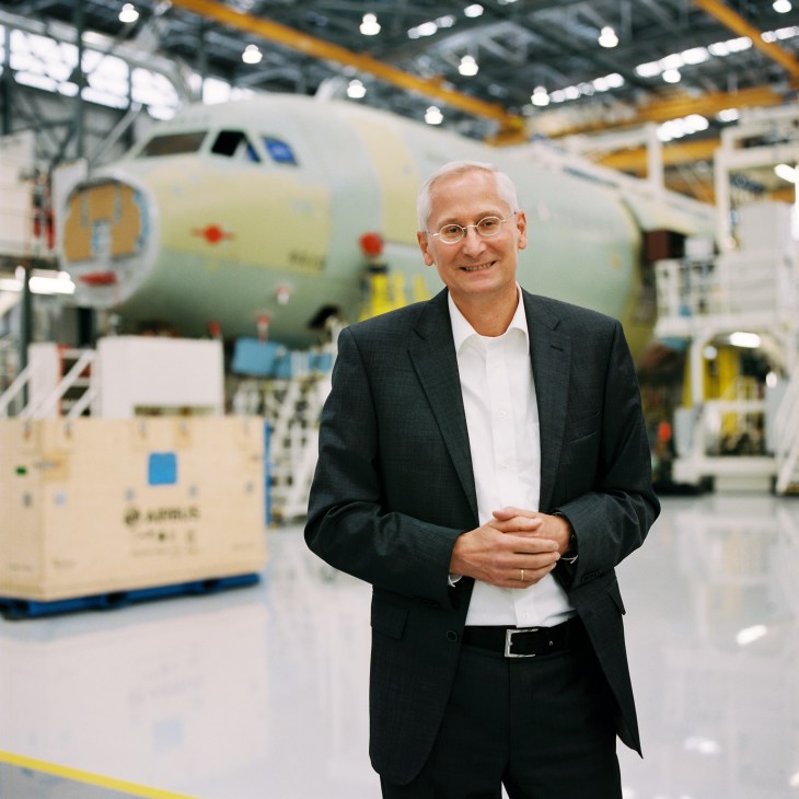 Dr Ulrich Weber stands in Airbus assembly facility with aircraft in background.