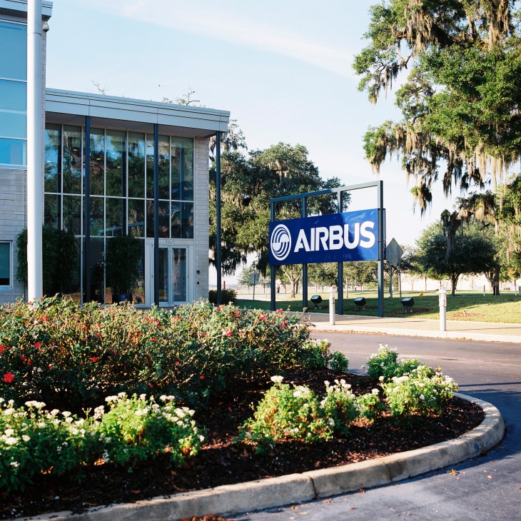 Airbus engineering centre in Mobile with blue signage, modern glass building, and landscaping with flowering shrubs.