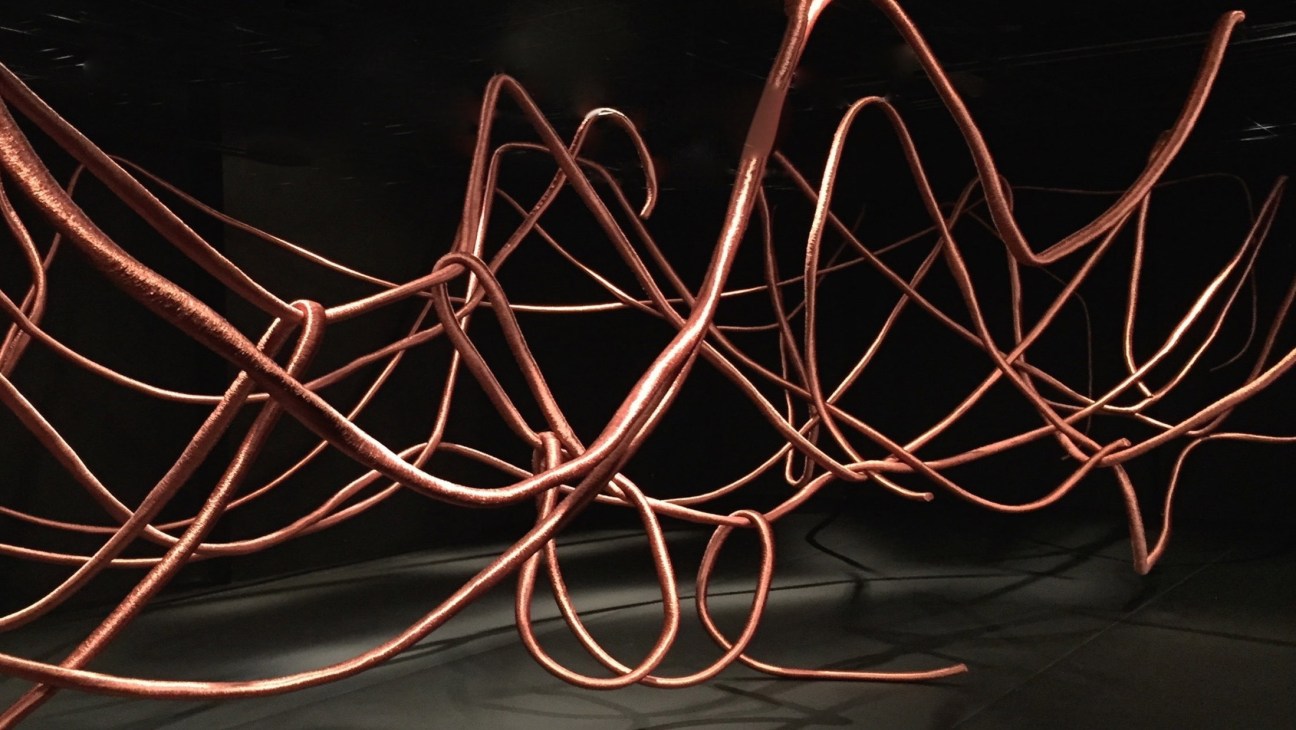 Copper-tinted sculptural cables forming abstract loops against a black background by Alice Anderson.