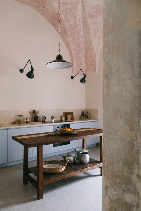 Palazzo Ventidue Puglia kitchen with high stone ceilings wooden table black lamps blue kitchen cupboards and pale pink alcoves