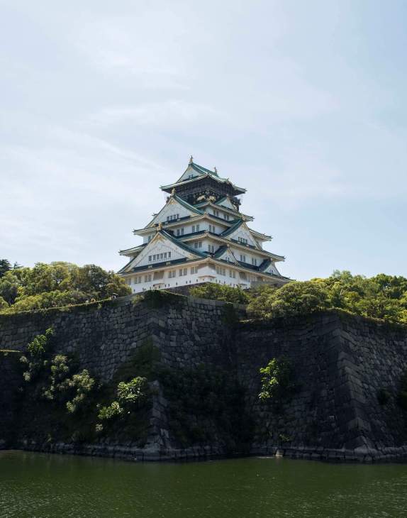 A photo of the Osaka castle with the castle wall and moat in the foreground.