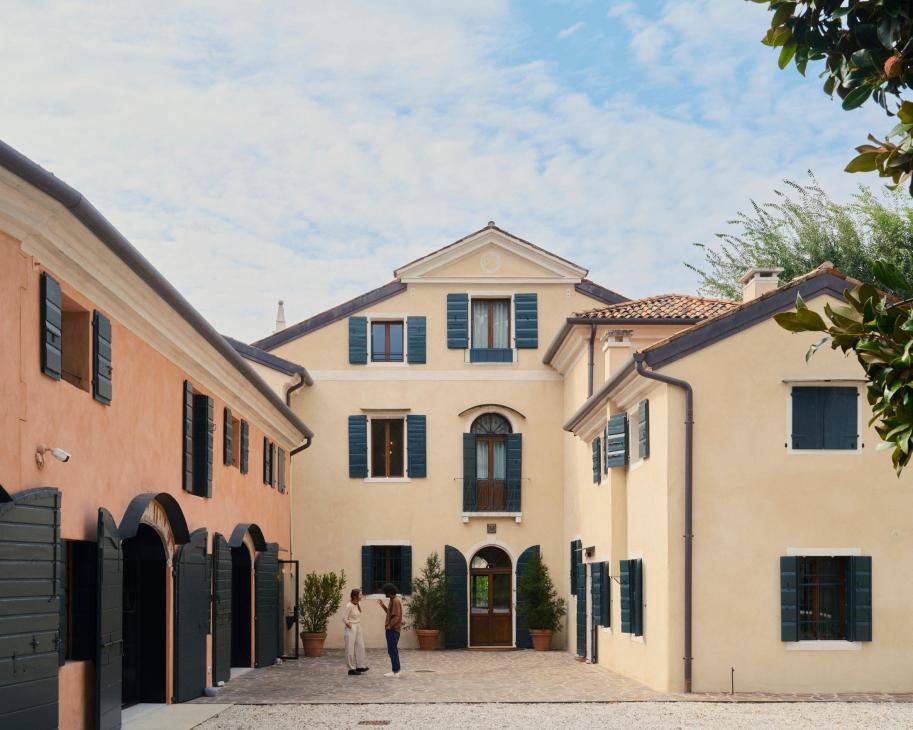 Exterior of an 18th-century Italian villa with cream-colored walls, blue shutters, and a courtyard entrance.