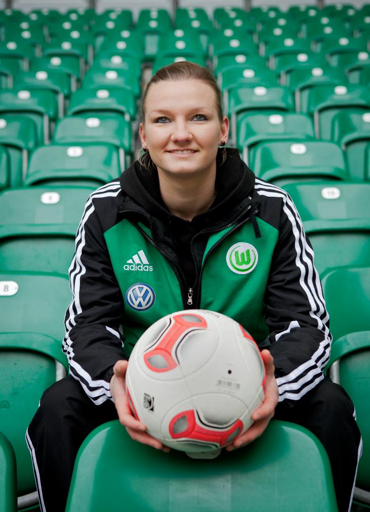 Alex Popp, German footballer for VfL Wolfsburg, holds a soccer ball while seated in stadium stands.