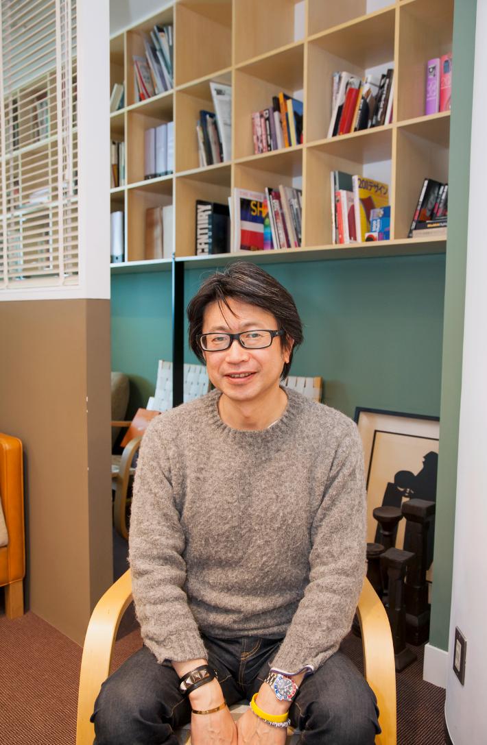 Kazuyoshi Minamimagoe, senior creative director of B:ming Life Store, sitting in front of wooden shelving.