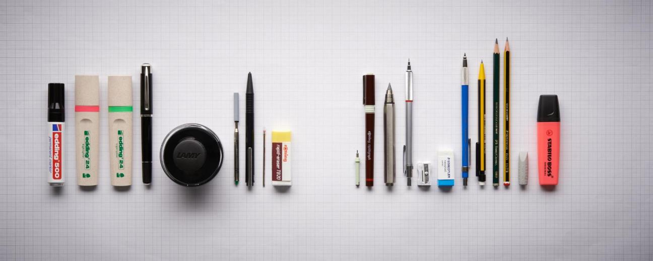 Collection of writing instruments including markers, pens, pencils, and erasers arranged on graph paper.