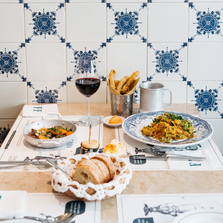 Food and wine on a table with wall tiles in the background.