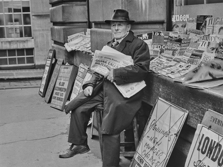 Vintage black and white photo of a man selling newspapers at a city newspaper stand