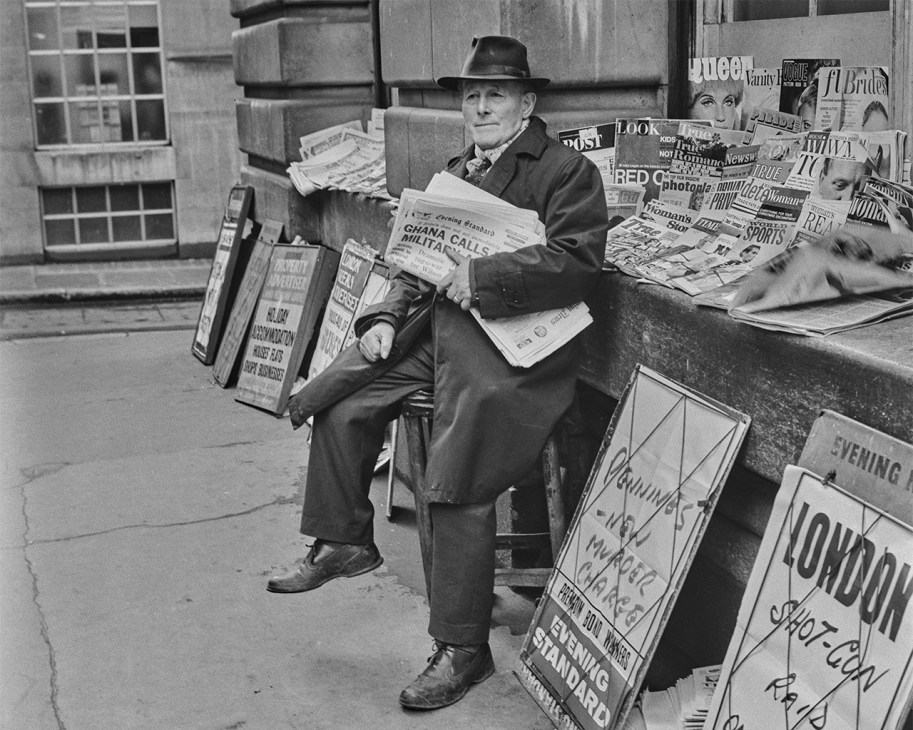 Vintage black and white photo of a man selling newspapers at a city newspaper stand