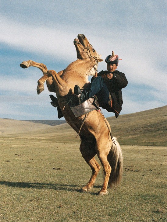 Man in A Kind of Guise clothing rides a rearing horse in the Mongolian Steppes