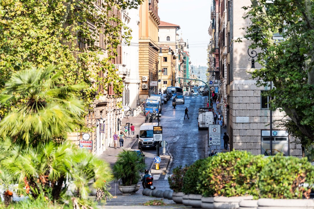 Rome, Italy - September 4, 2018: Streetscape of city town road Via Urbana sign and Piazza Esquilino park square, framing of street by green trees in Rioni Monti neighborhood