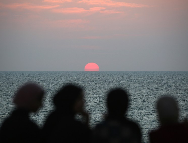 Displaced Palestinians watch the sunset as they spend time on the beach opposite their tents stretched along the Nuseirat beach road in the central Gaza Strip