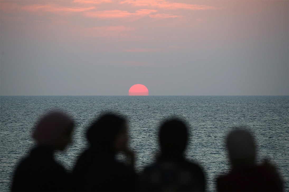 Displaced Palestinians watch the sunset as they spend time on the beach opposite their tents stretched along the Nuseirat beach road in the central Gaza Strip