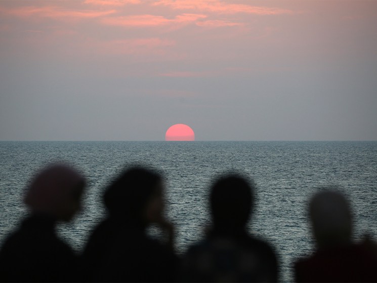 Displaced Palestinians watch the sunset as they spend time on the beach opposite their tents stretched along the Nuseirat beach road in the central Gaza Strip