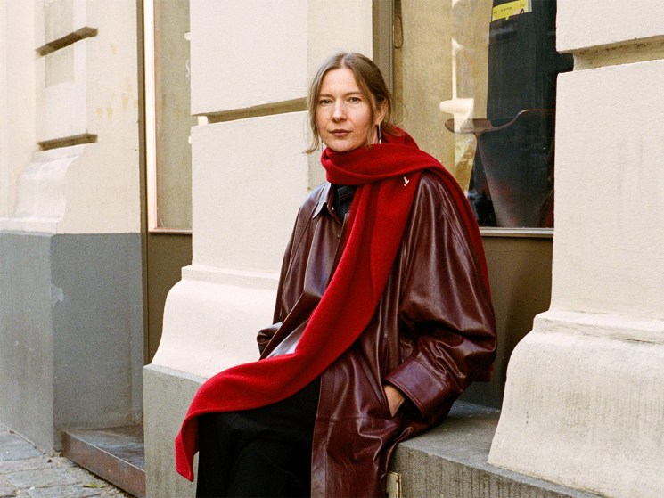 Tanja Bradaric of Sagan Vienna sits on a window sill in leather burgandy coat and red scarf