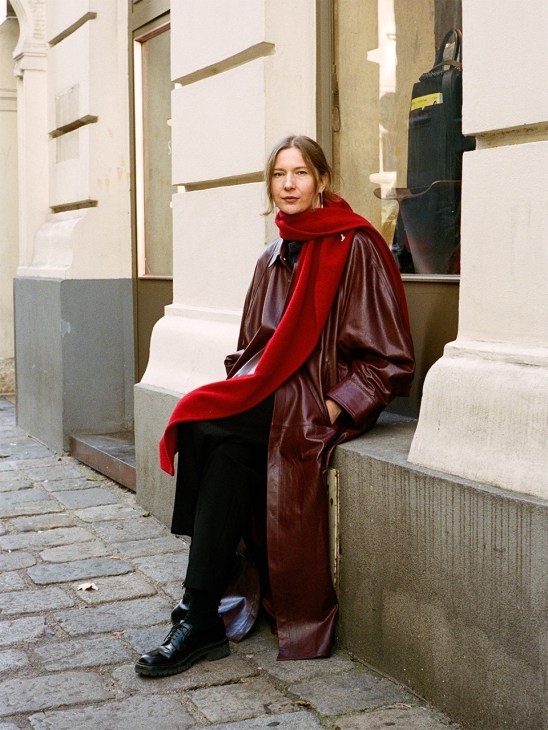 Tanja Bradaric of Sagan Vienna sits on a window sill in leather burgandy coat and red scarf