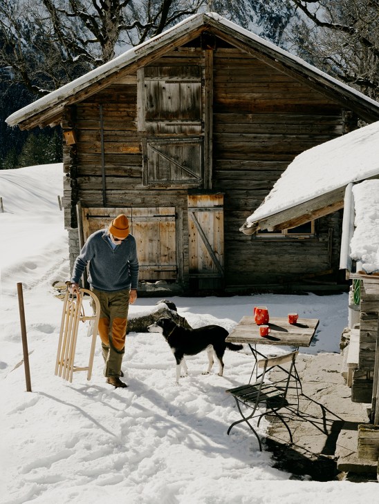 Man walks past snowy cabin holding a sledge