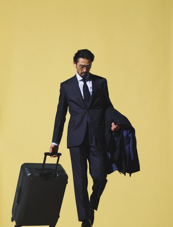 Model wearing jacket and trousers by Brioni, shirt and tie by Brunello Cucinelli, coat by Cahlumn, shoes by Crockett & Jones, glasses by Mykita, belt by Brady1A.H, suitcase by Proteca
