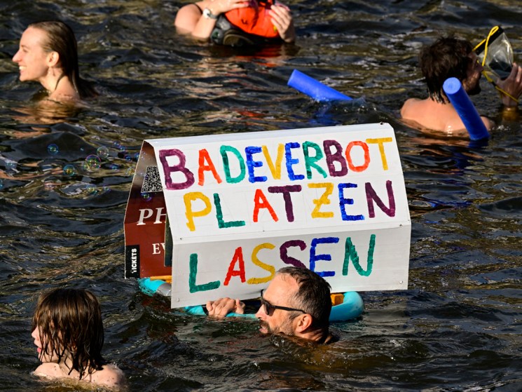 A participant swims with a placard with the lettering 'Break the bathing ban' while taking a dip in the Spree river during a second swimming demonstration for the abolition of the general swimming ban in the inner-city Spree river in central Berlin on August 12, 2025. They demonstrate for the possibility to swim in the inner-city Spree river again; it was banned around 100 years ago. (Photo by John MACDOUGALL / AFP) (Photo by JOHN MACDOUGALL/AFP via Getty Images)