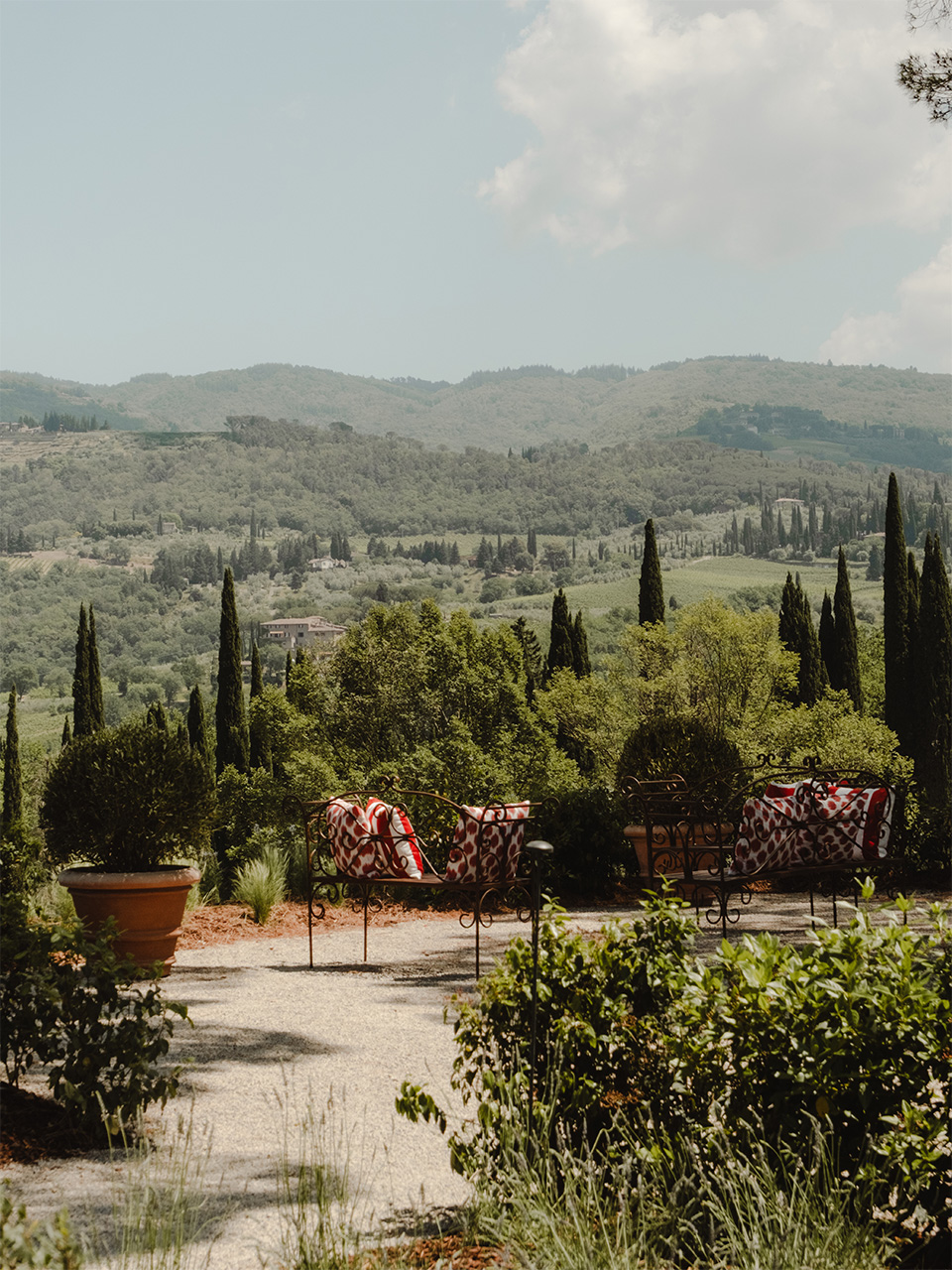 Tuscan terrace with patterned lounge chairs overlooking rolling Chianti hills dotted with cypress trees.
