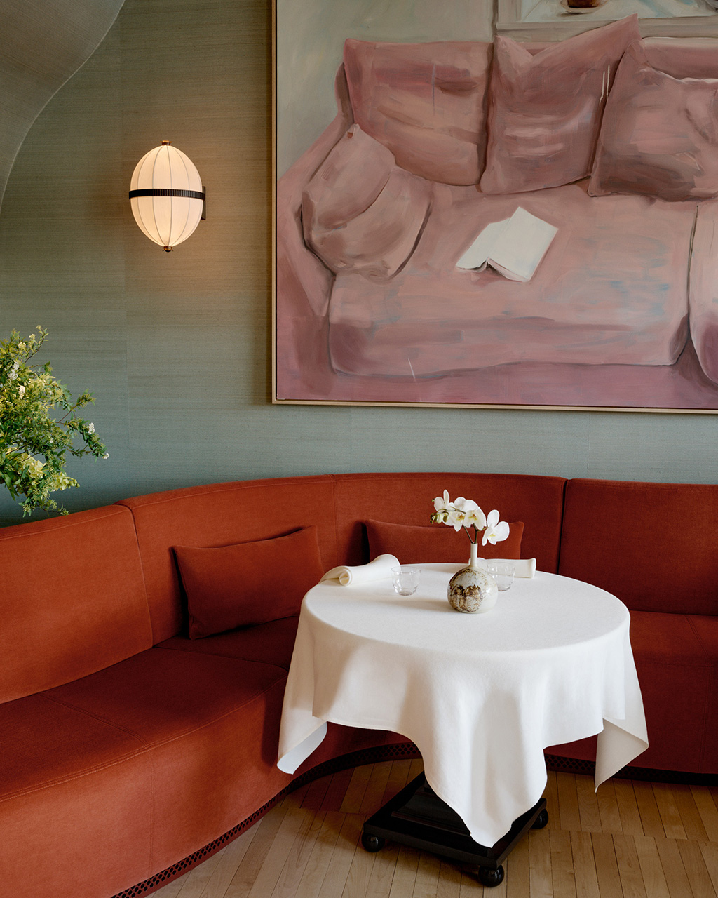 Modern restaurant interior with red curved banquette seating, round white table, and pink artwork on pale green wall