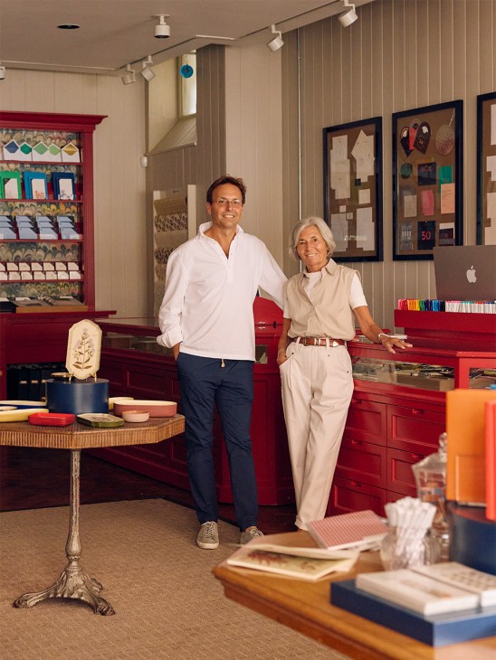 Alex Cain and his mother Fridette stand in Mount Street Printers' Mayfair shop lined with red display cabinets and paper samples.