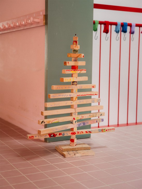 A Christmas tree made of stacked wooden blocks with handwritten text and decorative tape arranged in a tapered pyramid shape.