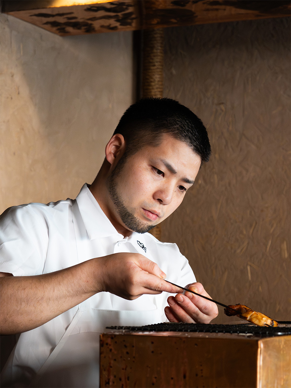 Chef in white chef's coat carefully plating a dish with a brush