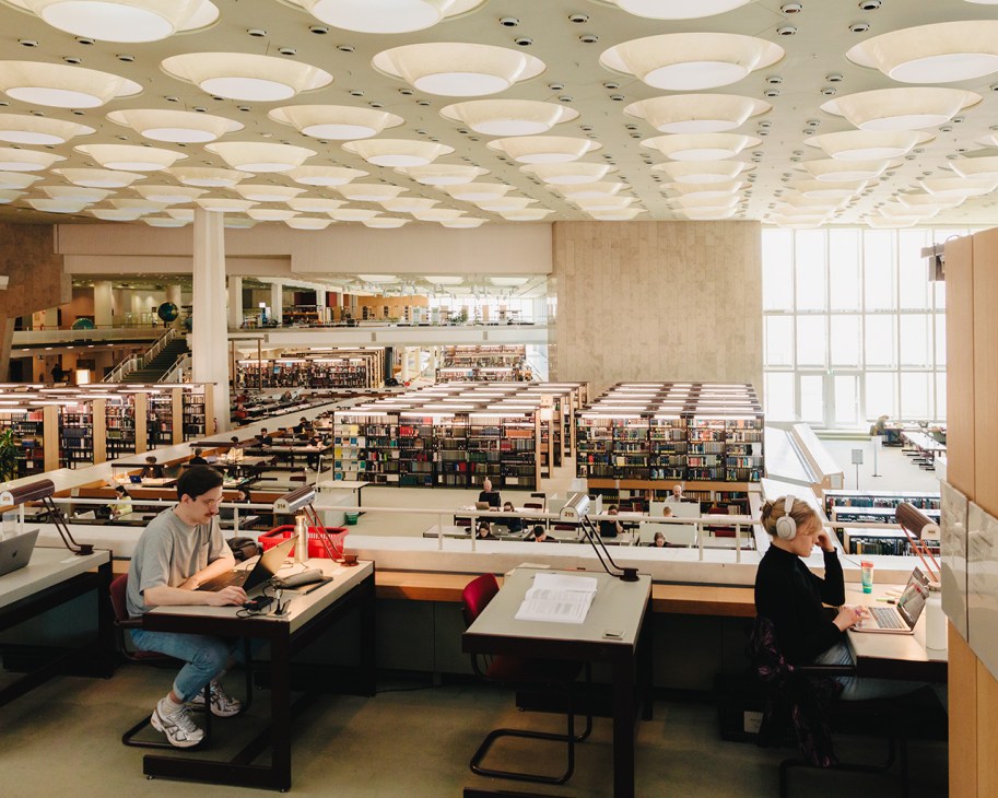 Readers study at desks in Berlin's Stabi library with bookshelves and multiple levels visible in the background.