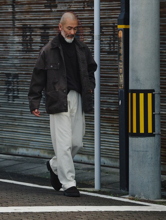Chef Shinichiro Harakawa wears a black Emporio Armani jacket, cream Kaptain Sunshine rollneck and trousers, and JM Weston shoes on an urban street.