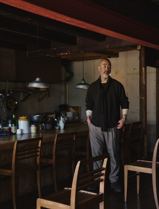 Chef Shinichiro Harakawa stands in a kitchen wearing a black Porter Classic jumper and scarf with Visvim shirt and Herno trousers.