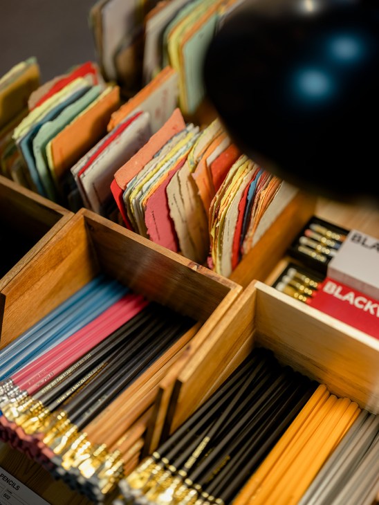 Papelaria colorida e lápis dispostos em expositores de madeira na loja O Momento.