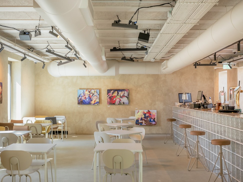 Interior of Primeiro Andar at Casa Capitão showing dining area with cream chairs, bar counter, artwork on walls, and exposed ceiling systems.