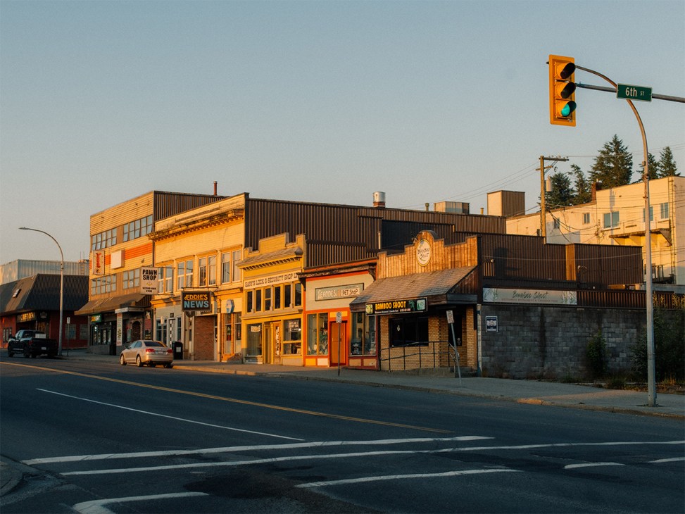 Street view of downtown Prince Rupert with yellow and orange-painted storefronts and a green 6th Street traffic light.