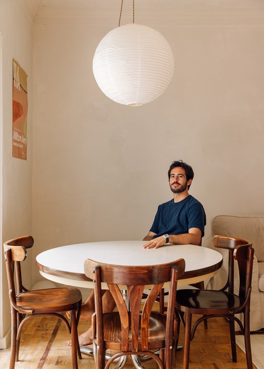 Architect José Guimarães sits at a round white table with wooden chairs beneath a hanging paper lantern in his converted Lisbon apartment.
