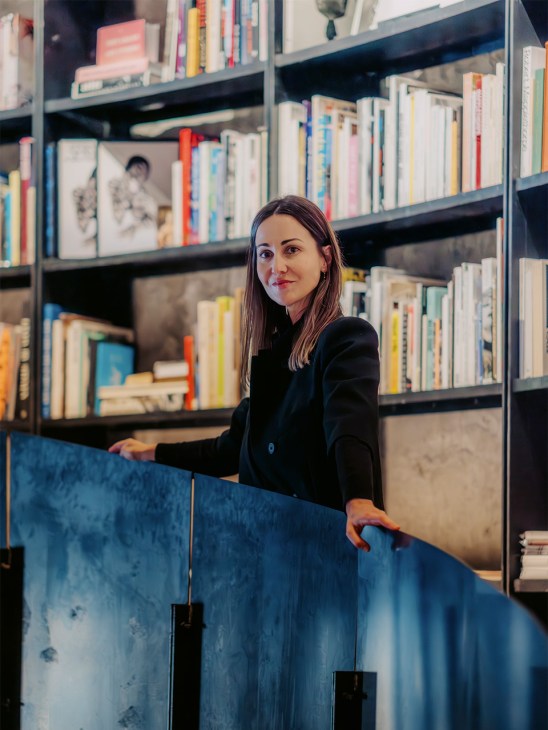 Letitia Castromil, director of the MOP Foundation, stands before floor-to-ceiling bookshelves in the library.